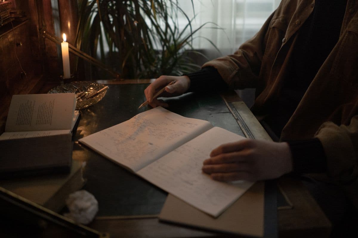 Hands writing by lamplight in an open notebook